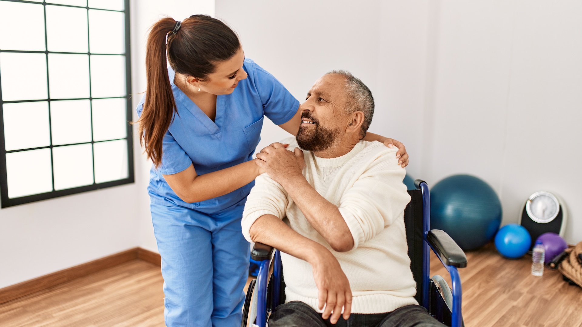 Senior man sitting on wheelchair and geriatric nurse at rehabilitation clinic